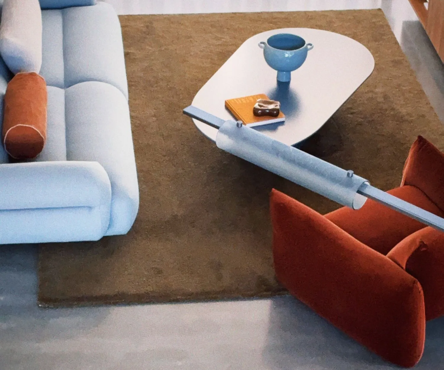 Overhead view of the powder blue sofa and rust armchairs around a white kidney-shaped coffee table on an ochre rug, a blue ceramic urn and an orange book on the table.